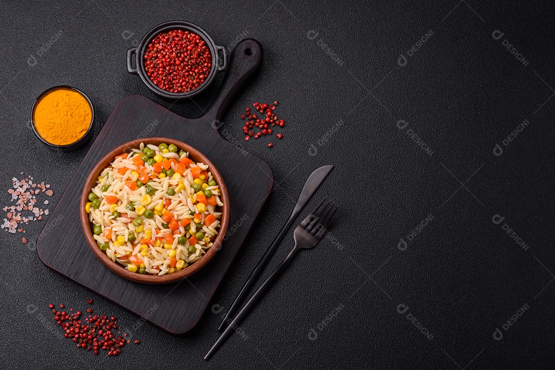 Delicioso arroz cozido com legumes milho, cenouras, ervilhas com sal, especiarias e ervas sobre um fundo escuro de concreto