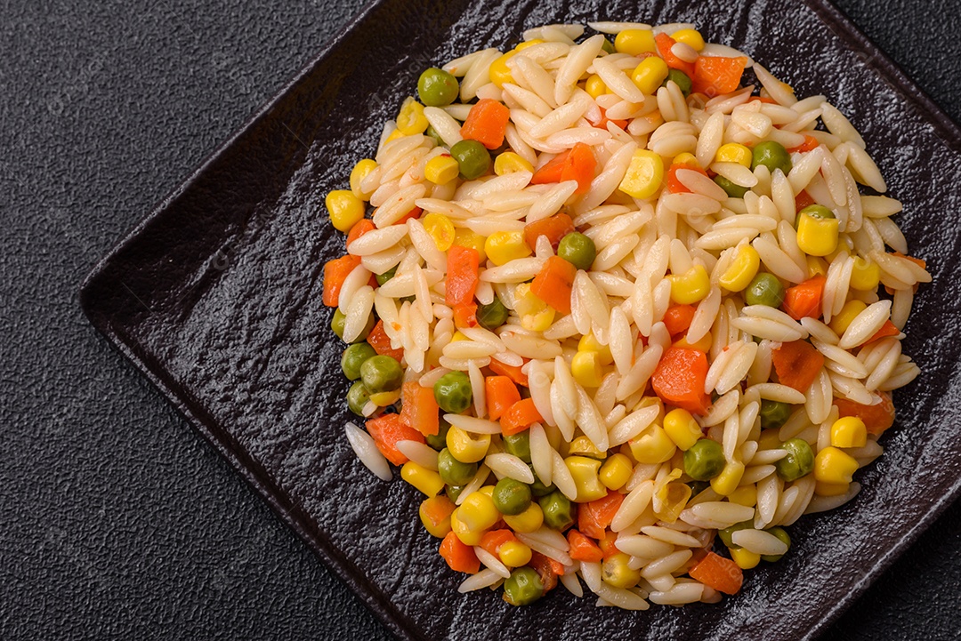 Delicioso arroz cozido com legumes milho, cenouras, ervilhas com sal, especiarias e ervas sobre um fundo escuro de concreto