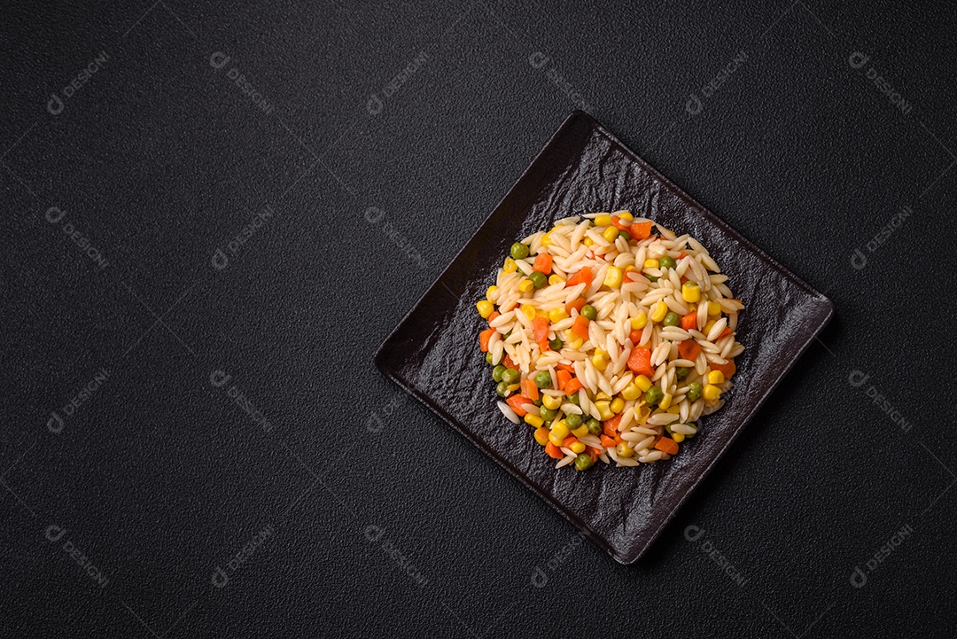 Delicioso arroz cozido com legumes milho, cenouras, ervilhas com sal, especiarias e ervas sobre um fundo escuro de concreto