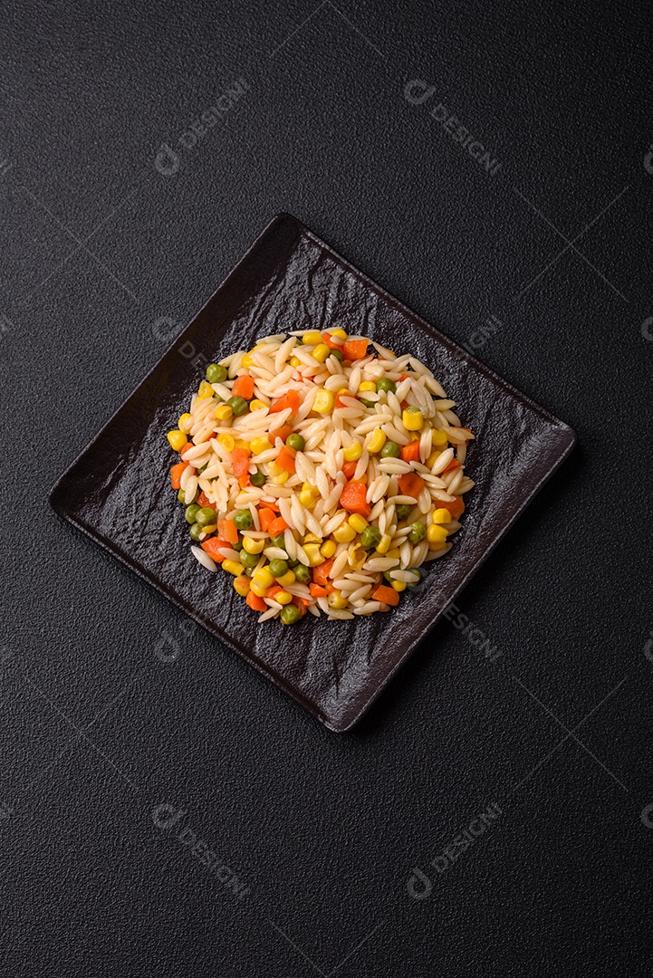 Delicioso arroz cozido com legumes milho, cenouras, ervilhas com sal, especiarias e ervas sobre um fundo escuro de concreto