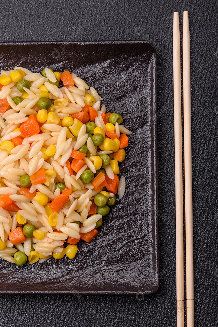Delicioso arroz cozido com legumes milho, cenouras, ervilhas com sal, especiarias e ervas sobre um fundo escuro de concreto