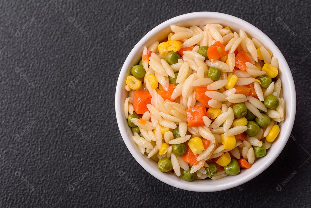 Delicioso arroz cozido com legumes milho, cenouras, ervilhas com sal, especiarias e ervas sobre um fundo escuro de concreto