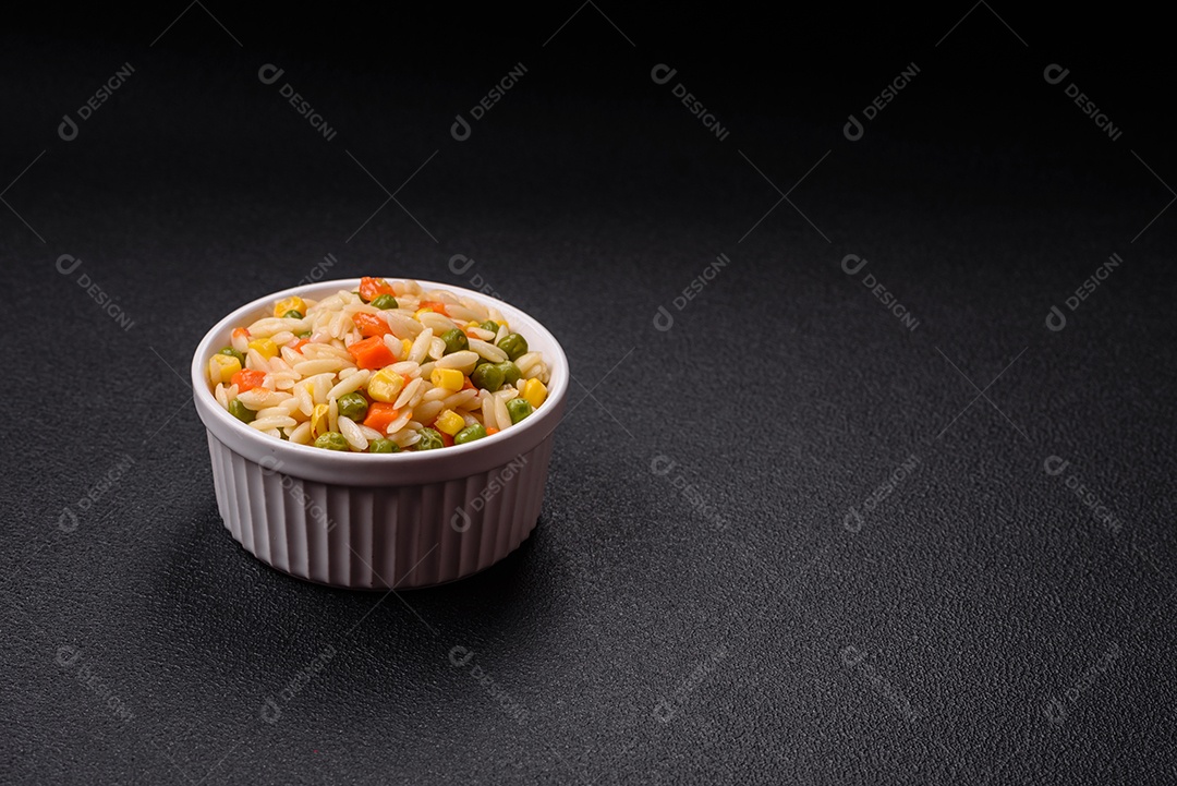 Delicioso arroz cozido com legumes milho, cenouras, ervilhas com sal, especiarias e ervas sobre um fundo escuro de concreto