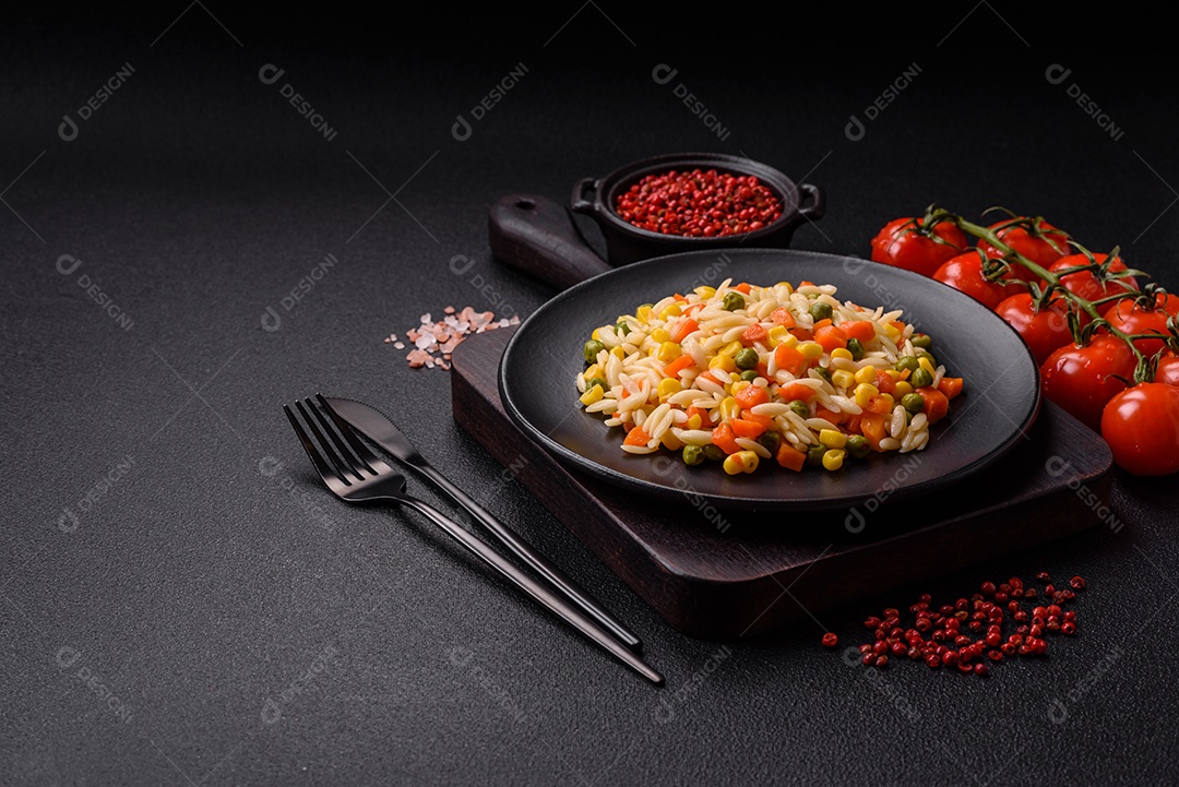 Delicioso arroz cozido com legumes milho, cenouras, ervilhas com sal, especiarias e ervas sobre um fundo escuro de concreto