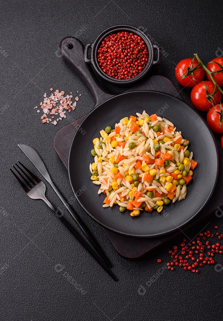 Delicioso arroz cozido com legumes milho, cenouras, ervilhas com sal, especiarias e ervas sobre um fundo escuro de concreto