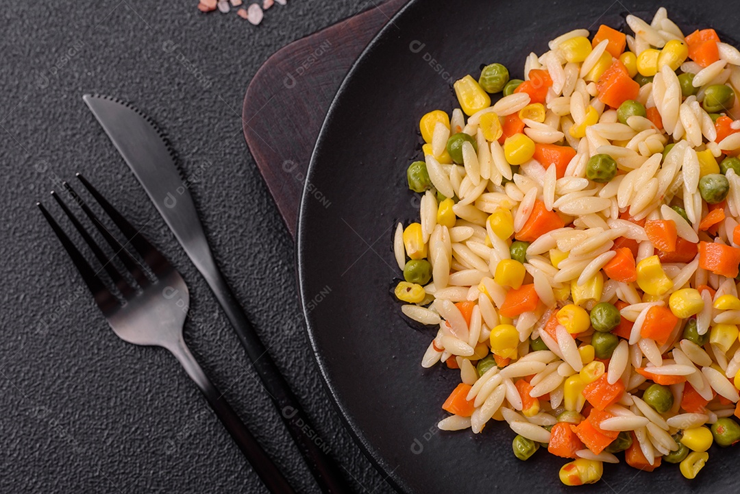 Delicioso arroz cozido com legumes milho, cenouras, ervilhas com sal, especiarias e ervas sobre um fundo escuro de concreto