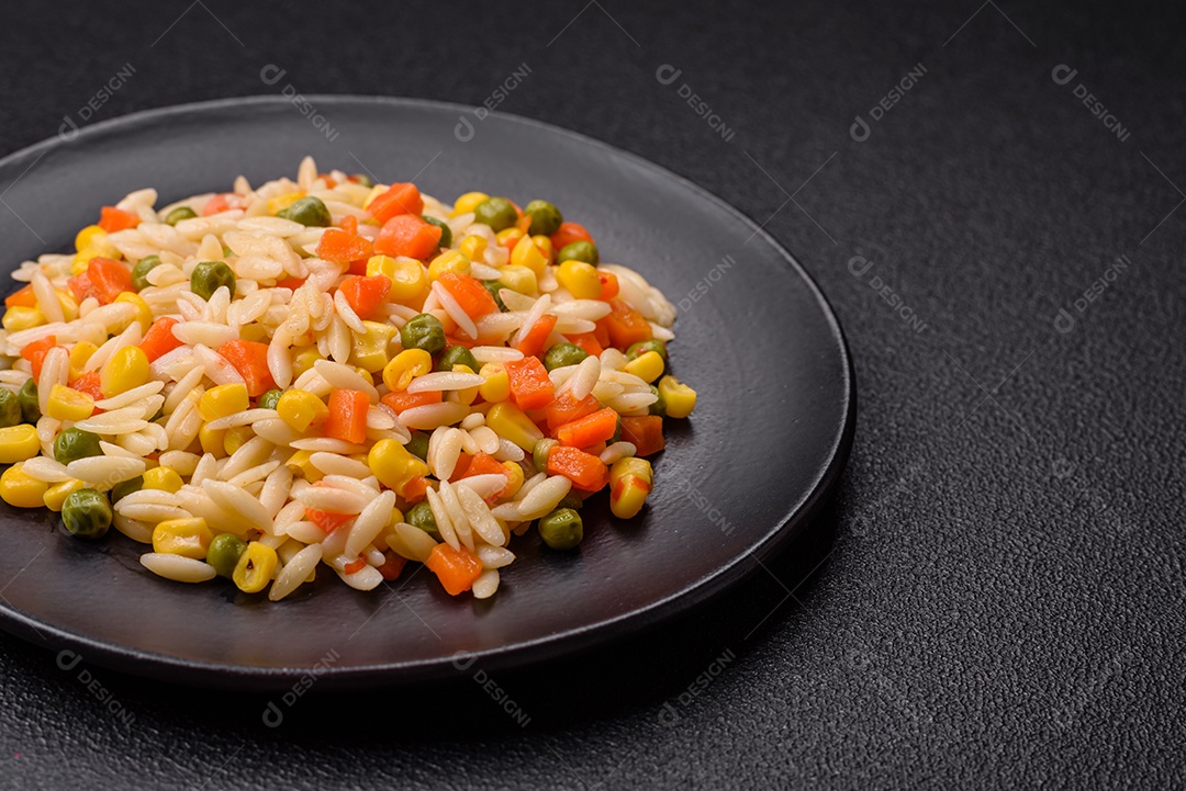 Delicioso arroz cozido com legumes milho, cenouras, ervilhas com sal, especiarias e ervas sobre um fundo escuro de concreto