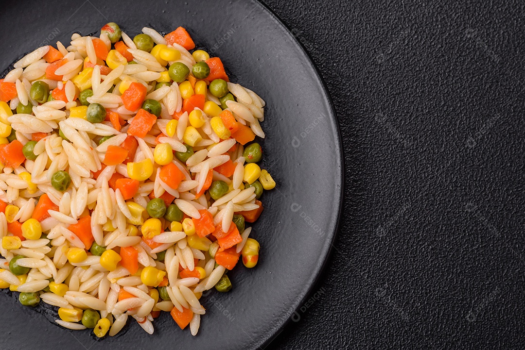 Delicioso arroz cozido com legumes milho, cenouras, ervilhas com sal, especiarias e ervas sobre um fundo escuro de concreto