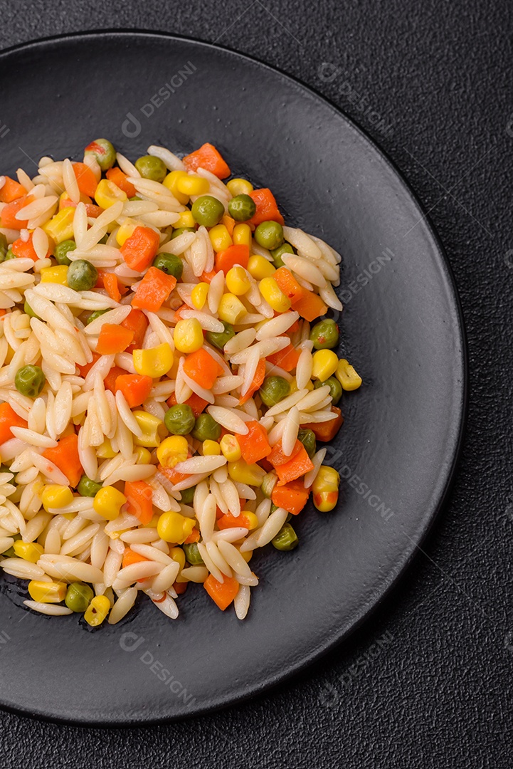 Delicioso arroz cozido com legumes milho, cenouras, ervilhas com sal, especiarias e ervas sobre um fundo escuro de concreto