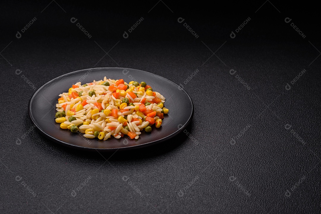 Delicioso arroz cozido com legumes milho, cenouras, ervilhas com sal, especiarias e ervas sobre um fundo escuro de concreto