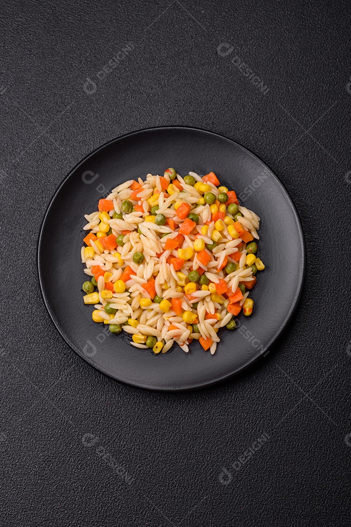 Delicioso arroz cozido com legumes milho, cenouras, ervilhas com sal, especiarias e ervas sobre um fundo escuro de concreto