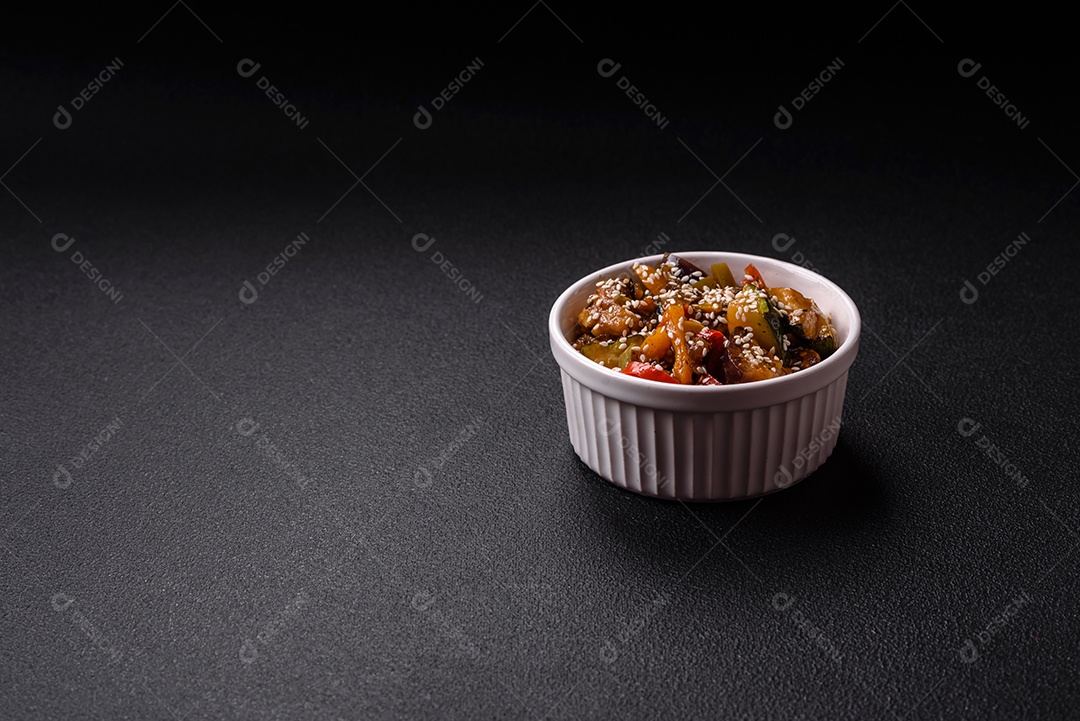 Prato asiático picante com filé de carne fatiado, pimenta, cenoura e sementes de gergelim sobre um fundo escuro de concreto