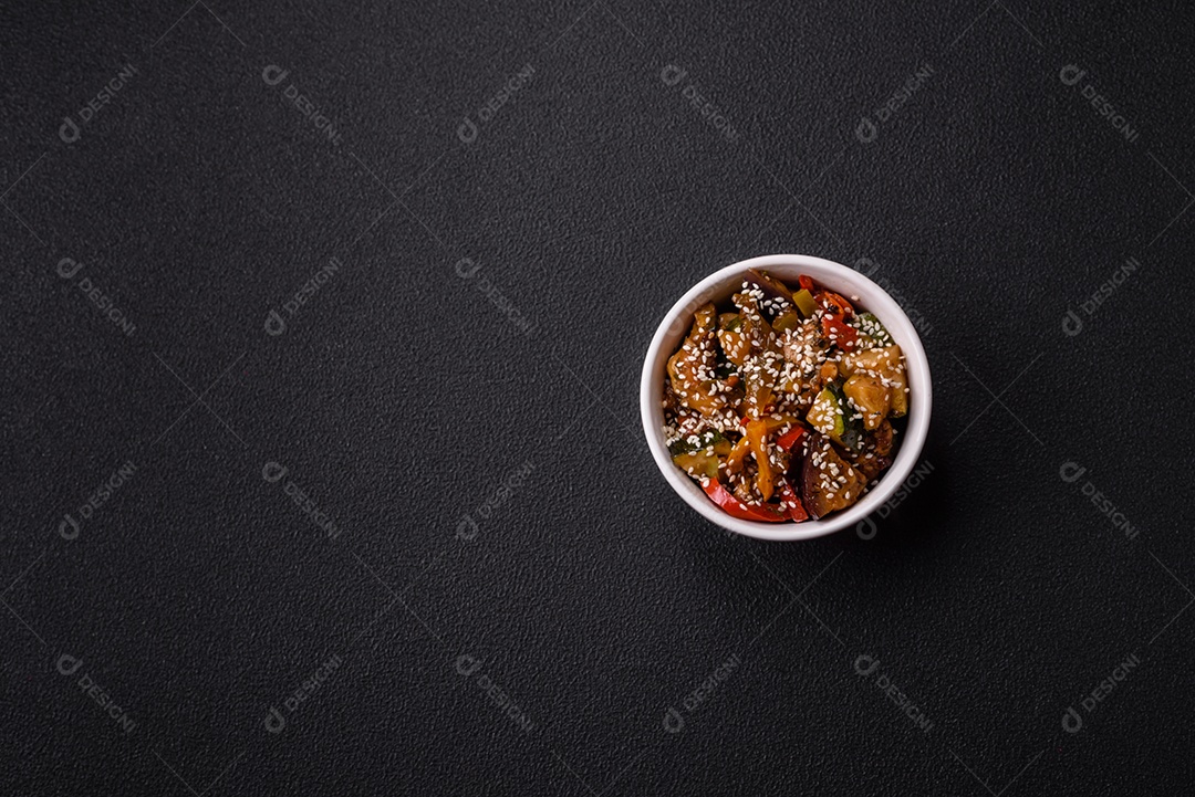 Prato asiático picante com filé de carne fatiado, pimenta, cenoura e sementes de gergelim sobre um fundo escuro de concreto