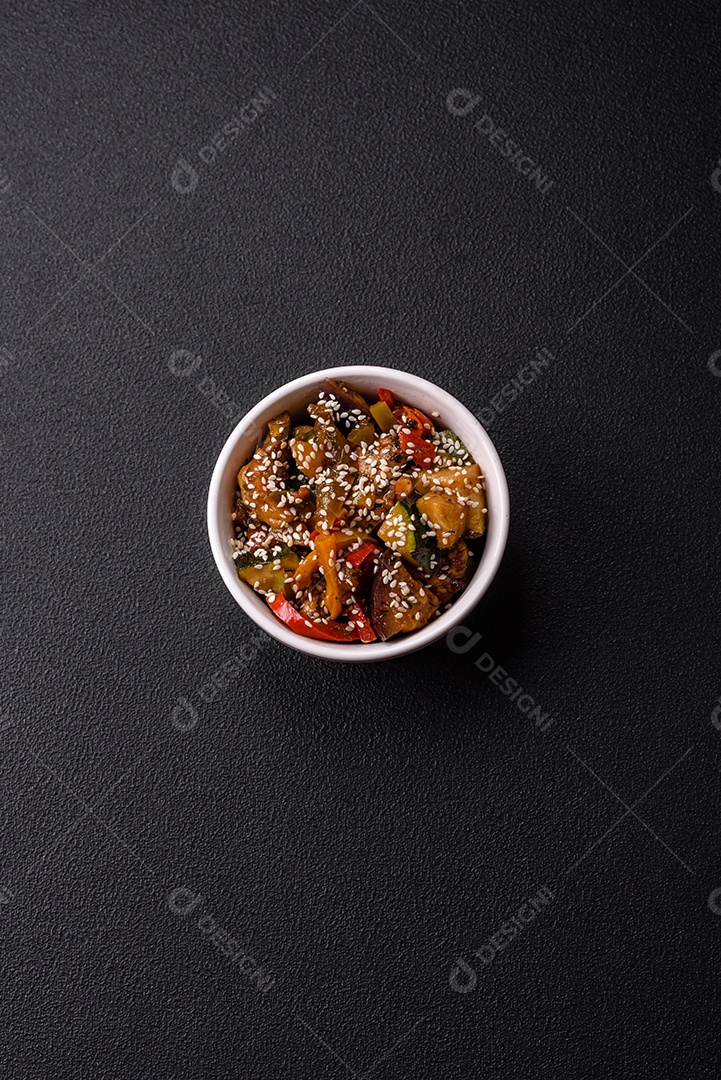 Prato asiático picante com filé de carne fatiado, pimenta, cenoura e sementes de gergelim sobre um fundo escuro de concreto