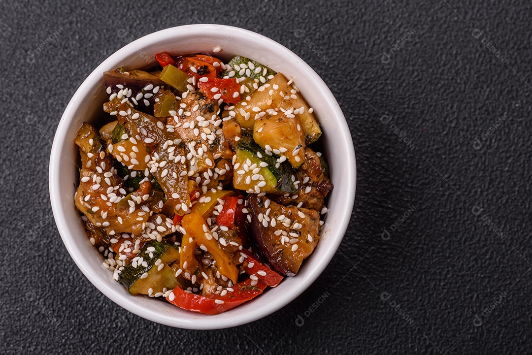 Prato asiático picante com filé de carne fatiado, pimenta, cenoura e sementes de gergelim sobre um fundo escuro de concreto