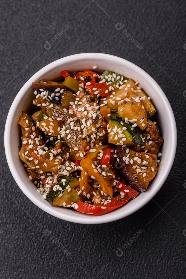 Prato asiático picante com filé de carne fatiado, pimenta, cenoura e sementes de gergelim sobre um fundo escuro de concreto