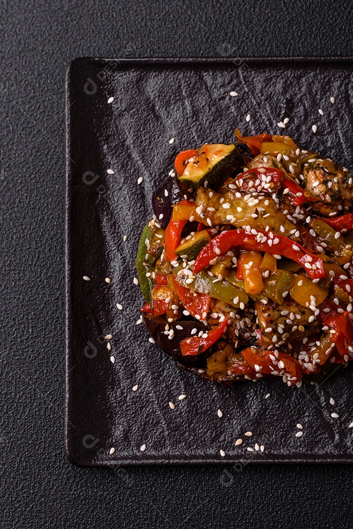 Prato asiático picante com filé de carne fatiado, pimenta, cenoura e sementes de gergelim sobre um fundo escuro de concreto