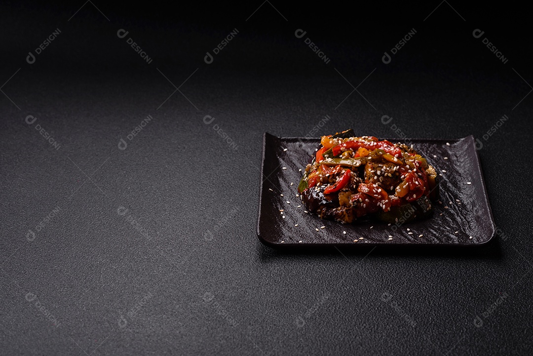 Prato asiático picante com filé de carne fatiado, pimenta, cenoura e sementes de gergelim sobre um fundo escuro de concreto