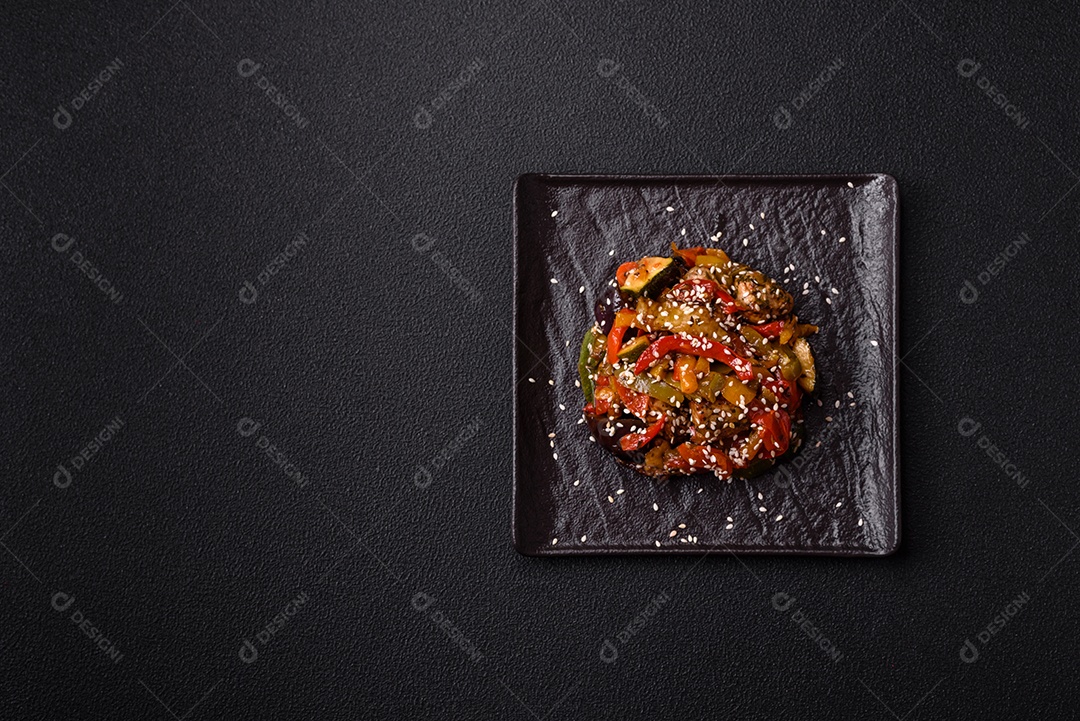 Prato asiático picante com filé de carne fatiado, pimenta, cenoura e sementes de gergelim sobre um fundo escuro de concreto