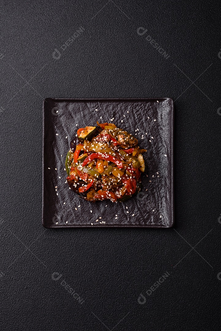 Prato asiático picante com filé de carne fatiado, pimenta, cenoura e sementes de gergelim sobre um fundo escuro de concreto