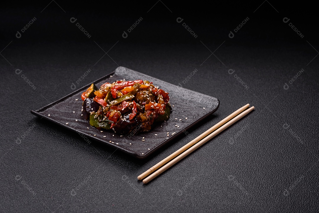 Prato asiático picante com filé de carne fatiado, pimenta, cenoura e sementes de gergelim sobre um fundo escuro de concreto