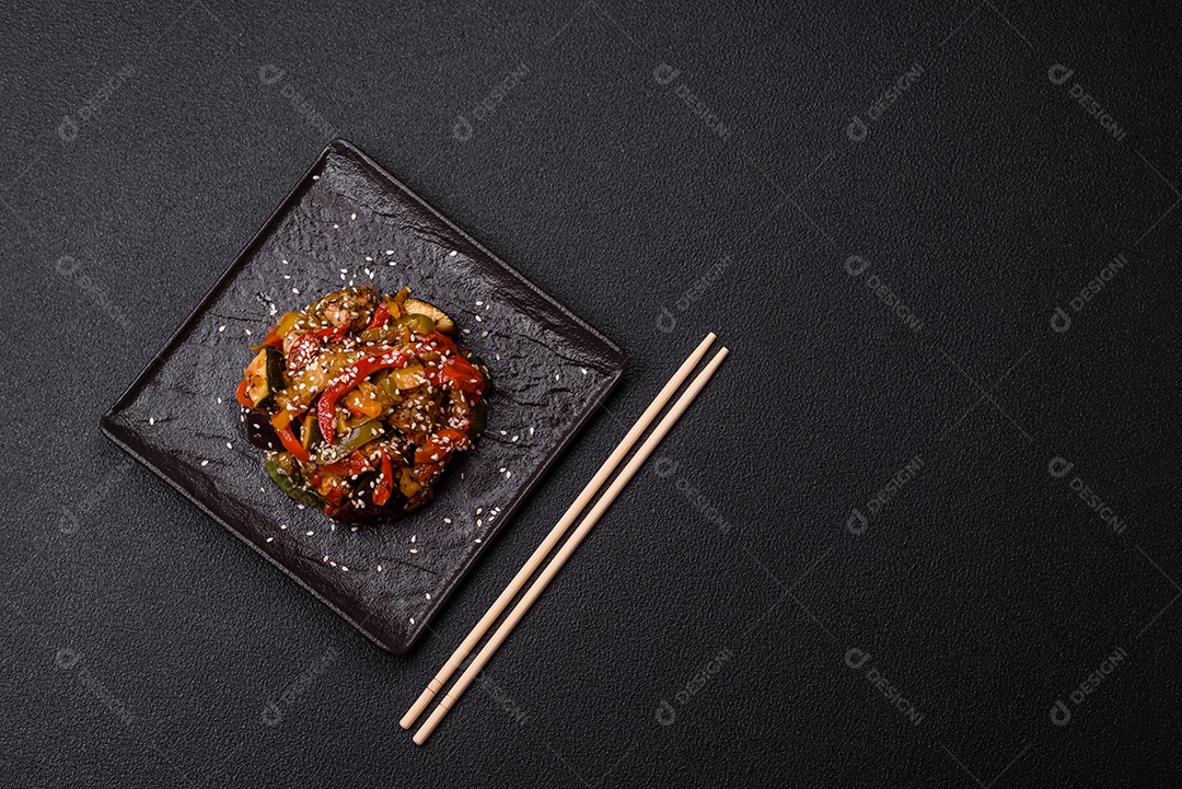 Prato asiático picante com filé de carne fatiado, pimenta, cenoura e sementes de gergelim sobre um fundo escuro de concreto