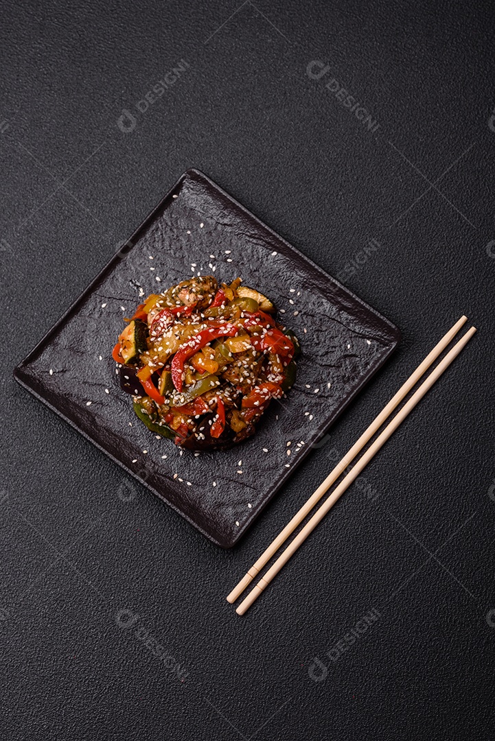 Prato asiático picante com filé de carne fatiado, pimenta, cenoura e sementes de gergelim sobre um fundo escuro de concreto