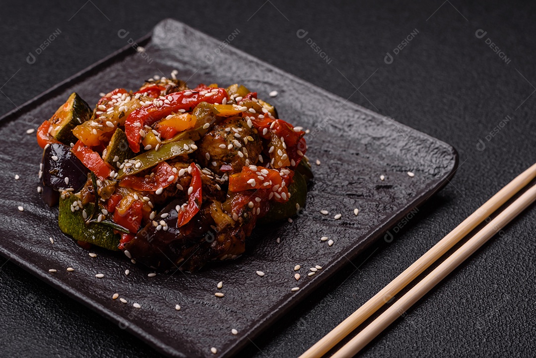 Prato asiático picante com filé de carne fatiado, pimenta, cenoura e sementes de gergelim sobre um fundo escuro de concreto