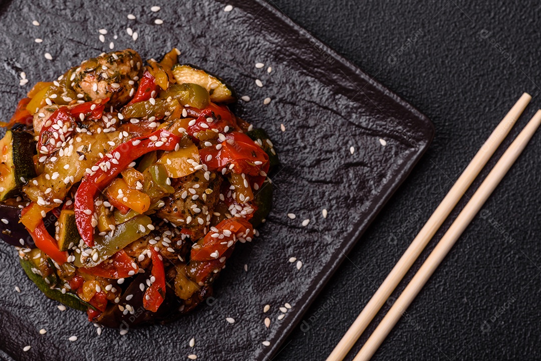 Prato asiático picante com filé de carne fatiado, pimenta, cenoura e sementes de gergelim sobre um fundo escuro de concreto