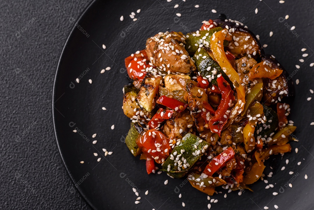 Prato asiático picante com filé de carne fatiado, pimenta, cenoura e sementes de gergelim sobre um fundo escuro de concreto