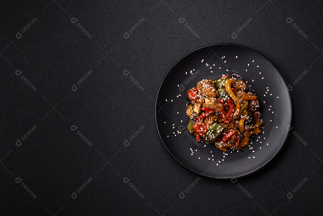 Prato asiático picante com filé de carne fatiado, pimenta, cenoura e sementes de gergelim sobre um fundo escuro de concreto
