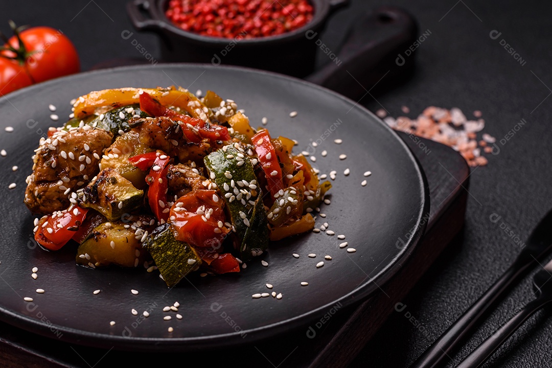 Prato asiático picante com filé de carne fatiado, pimenta, cenoura e sementes de gergelim sobre um fundo escuro de concreto