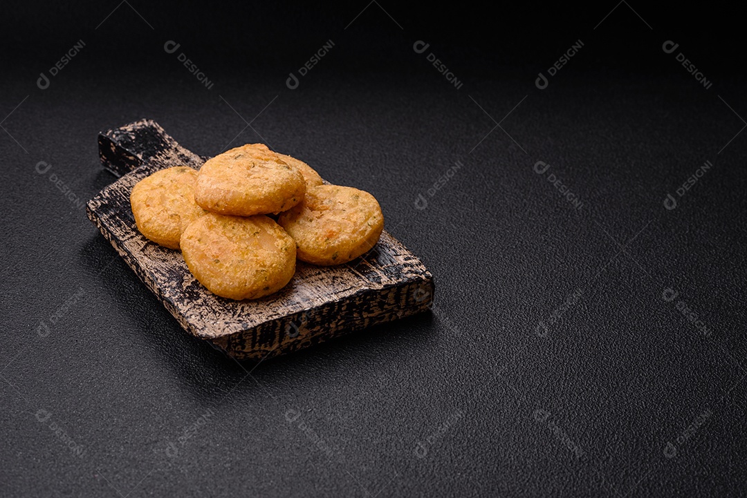 Peixe redondo ou pepitas de frango com sal e especiarias empanadas sobre um fundo escuro de concreto