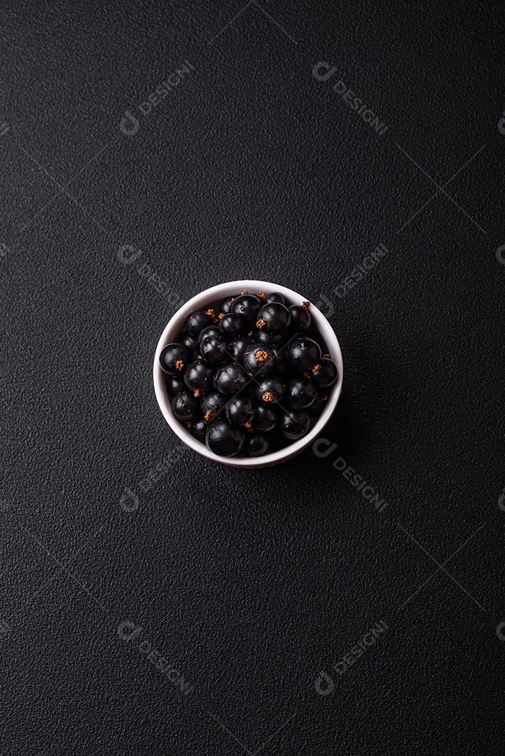Bagas maduras de groselha preta em gotas de água em uma tigela de cerâmica sobre um fundo escuro de concreto
