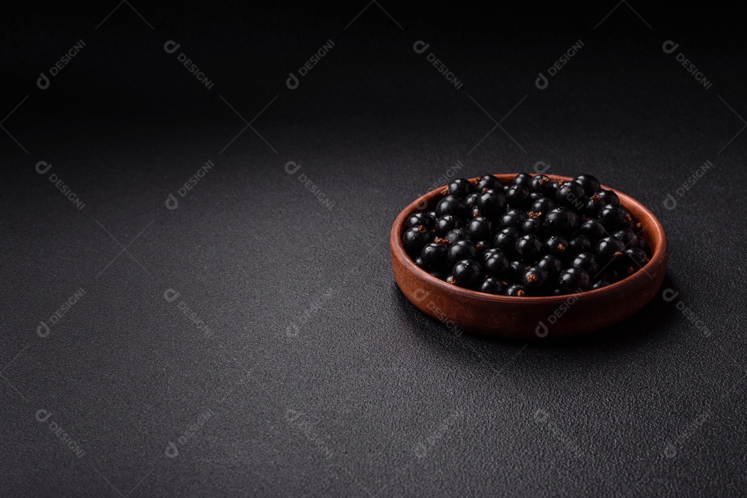 Bagas maduras de groselha preta em gotas de água em uma tigela de cerâmica sobre um fundo escuro de concreto