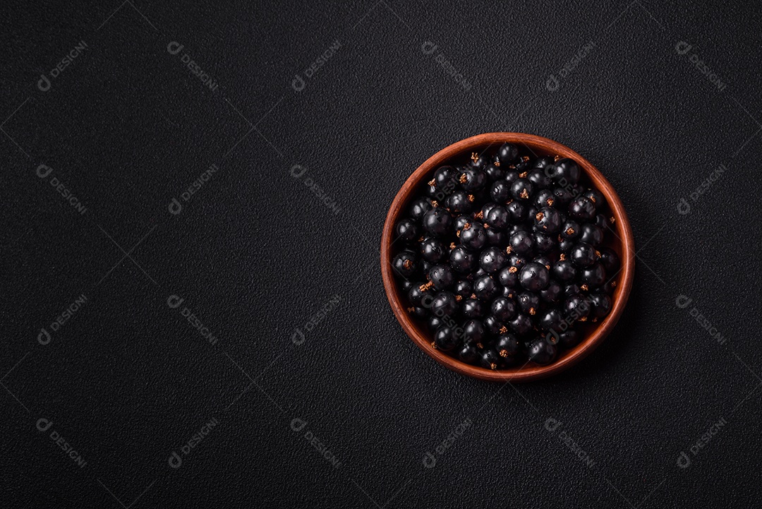 Bagas maduras de groselha preta em gotas de água em uma tigela de cerâmica sobre um fundo escuro de concreto