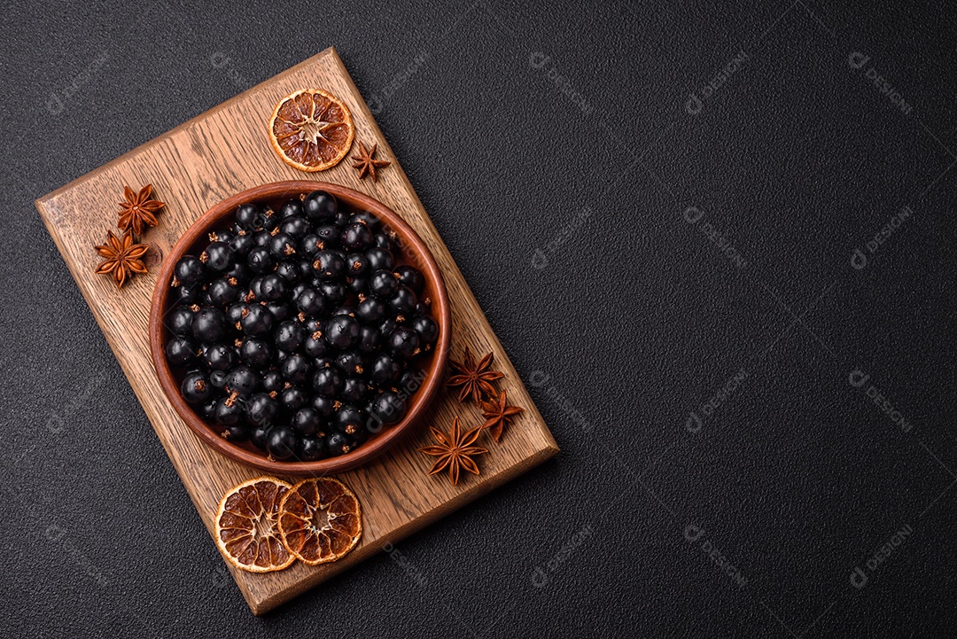 Bagas maduras de groselha preta em gotas de água em uma tigela de cerâmica sobre um fundo escuro de concreto