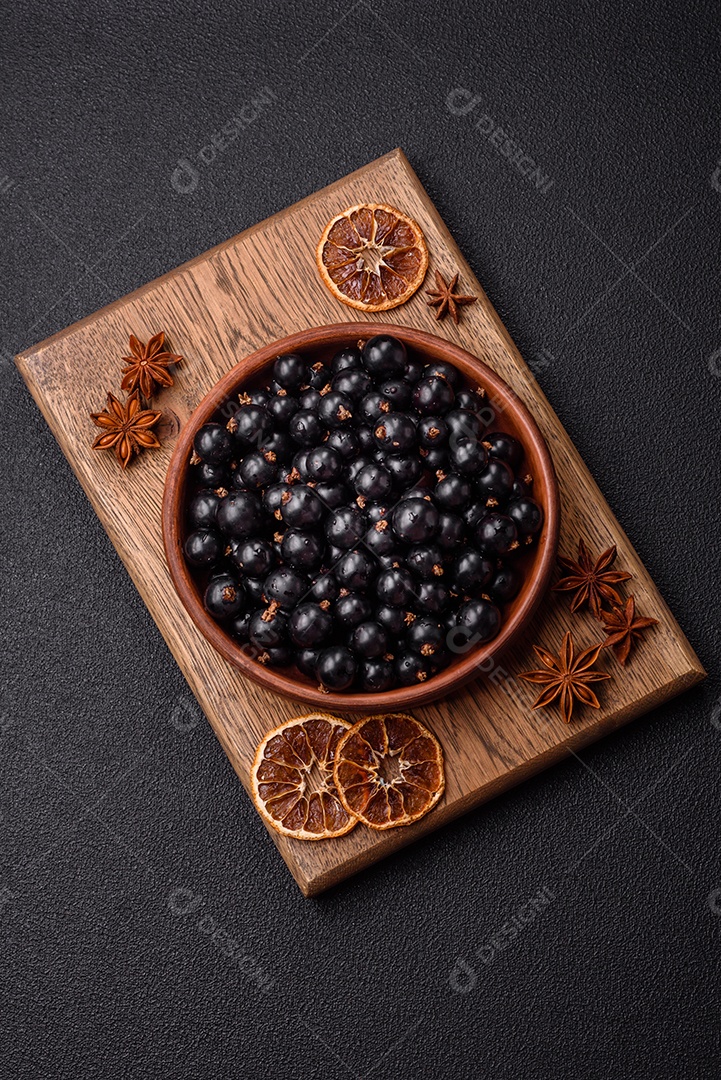 Bagas maduras de groselha preta em gotas de água em uma tigela de cerâmica sobre um fundo escuro de concreto