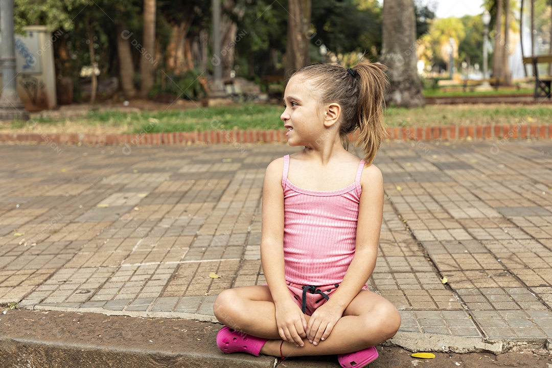 Linda garotinha sentada olhando para o lado em parque