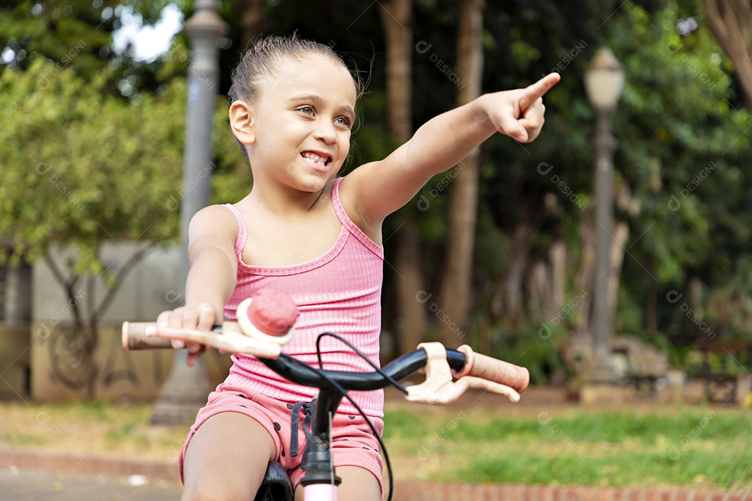 Linda garotinha mostrando algo na sua bicicleta