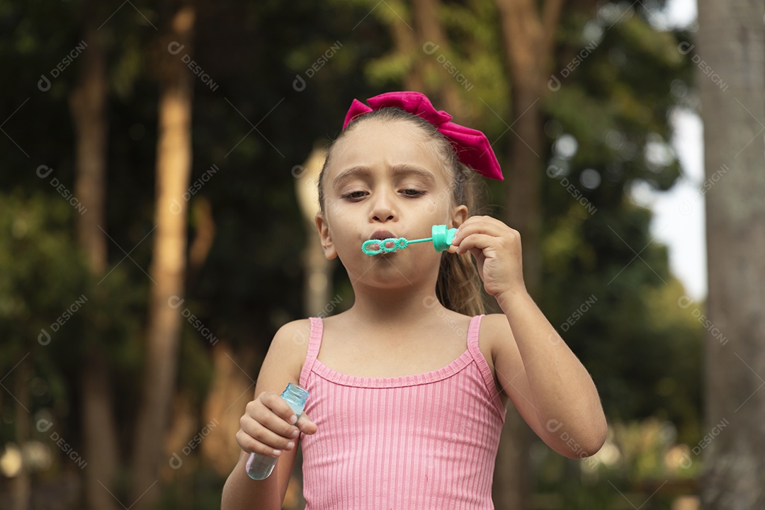 Uma adorável menina brincando no parque com bolhas de sabão