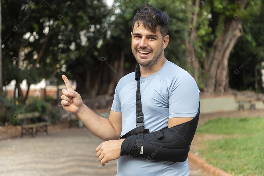 Homem sorrindo apontando para algo com braço na tipoia