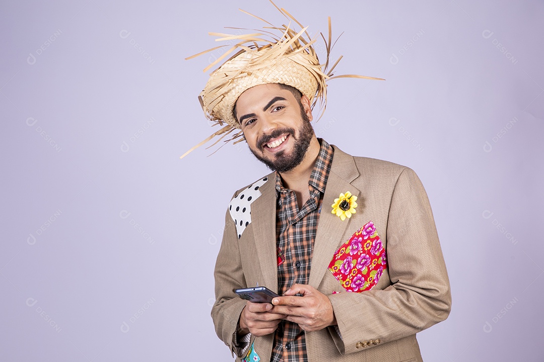 Jovem rapaz trajado para festa junina sorrindo com celular na mão