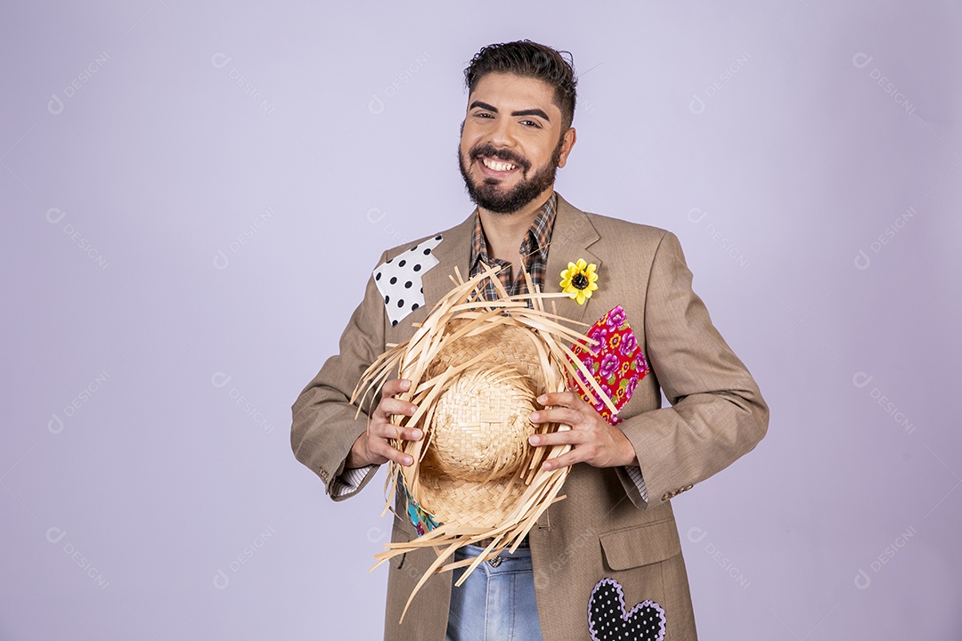 Jovem quadrilheiro animado para festa junina segurando chapéu nas mãos