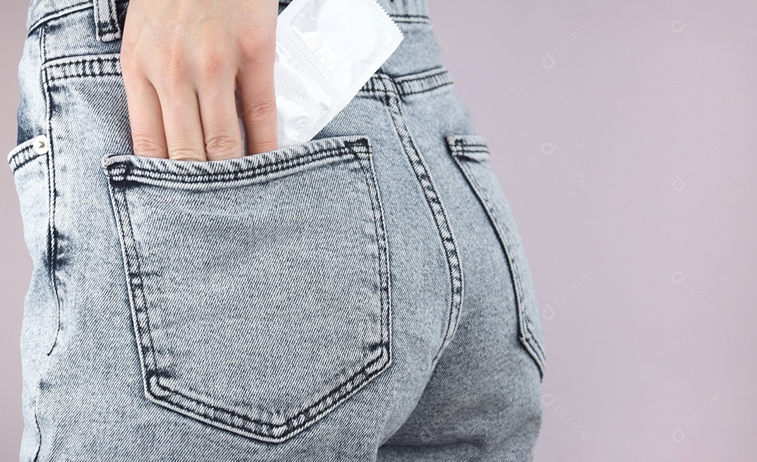 Mão feminina guardando camisinha no bolso de jeans