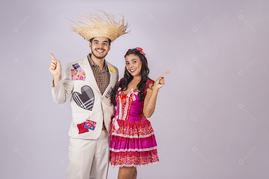 Casal de quadrilheiros trajados para festa junina apontando para os lados