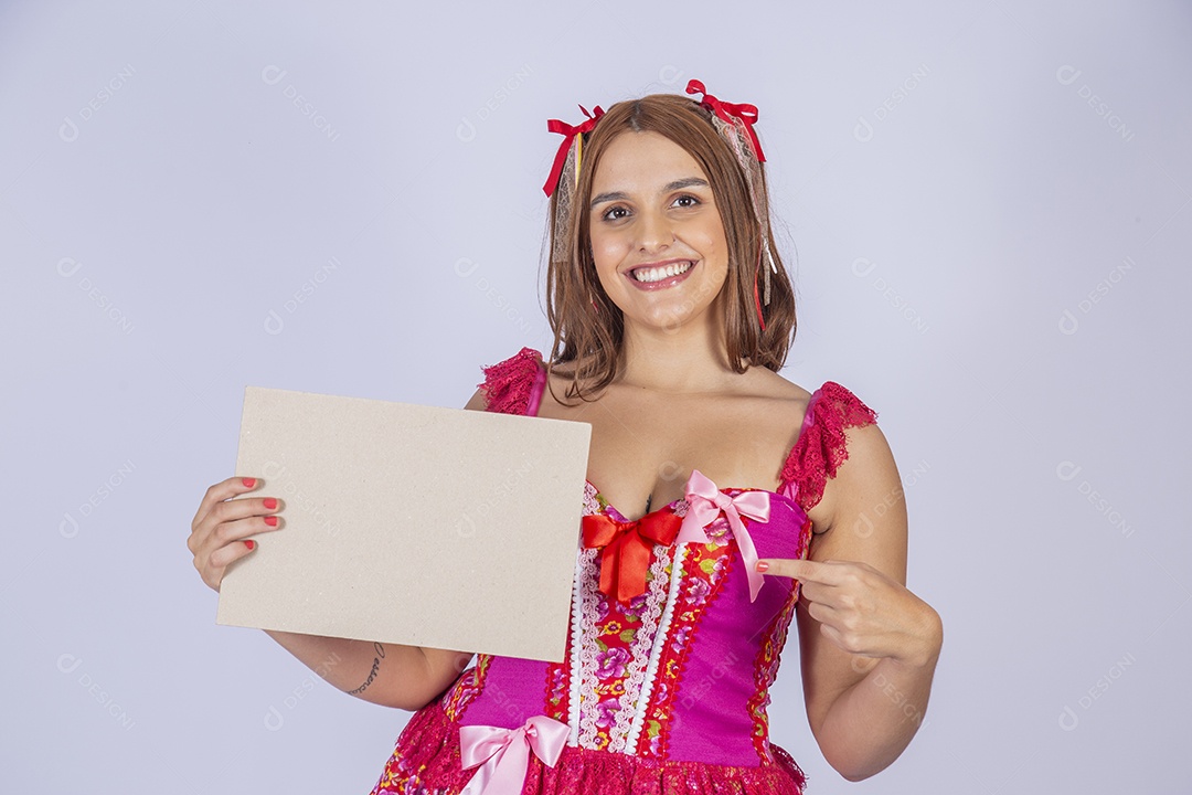 Jovem quadrilheira sorrindo e com trajes para festa junina com plaquinha