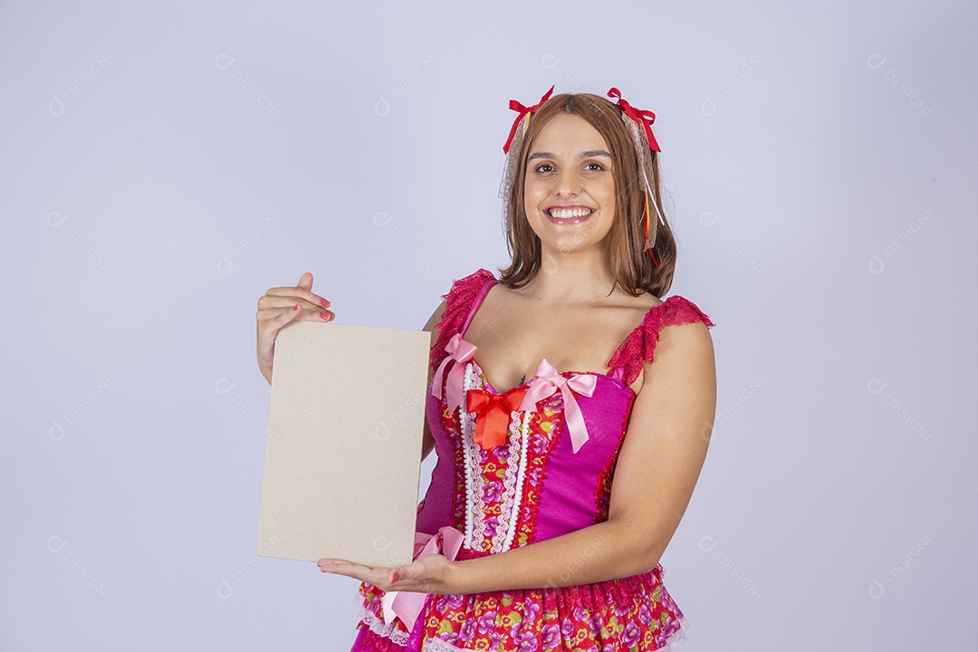 Jovem quadrilheira sorrindo e com trajes para festa junina com plaquinha
