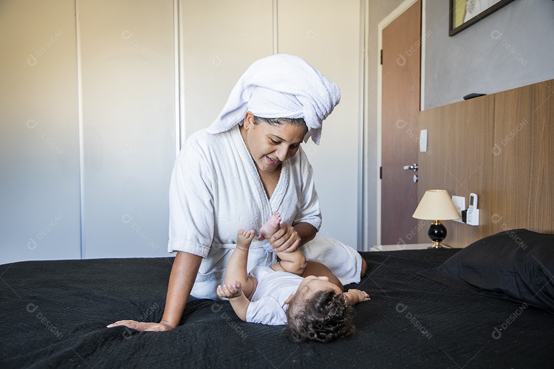 Mãe contente olhando e segurando seu bebê na cama