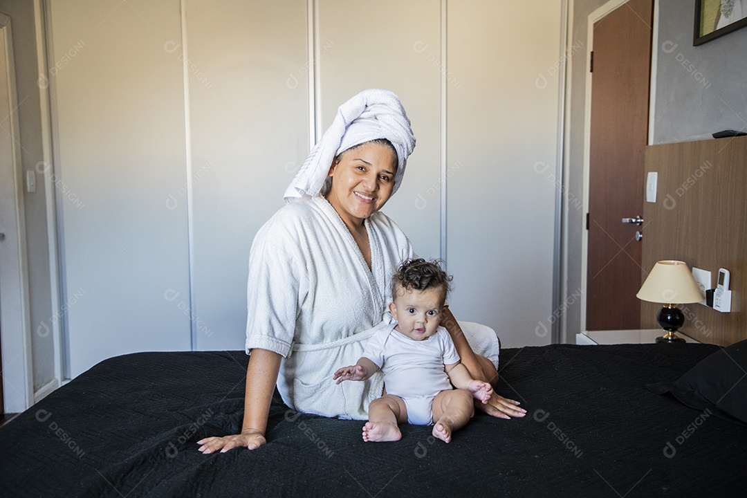 Mãe e seu bebê após banho sentados na cama